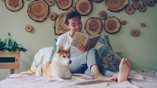A girl reads with her dog on the bed.
